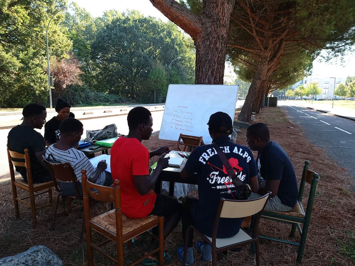 Mineurs isolés entrain d'étudier entre eux en plein air, sous un arbre.